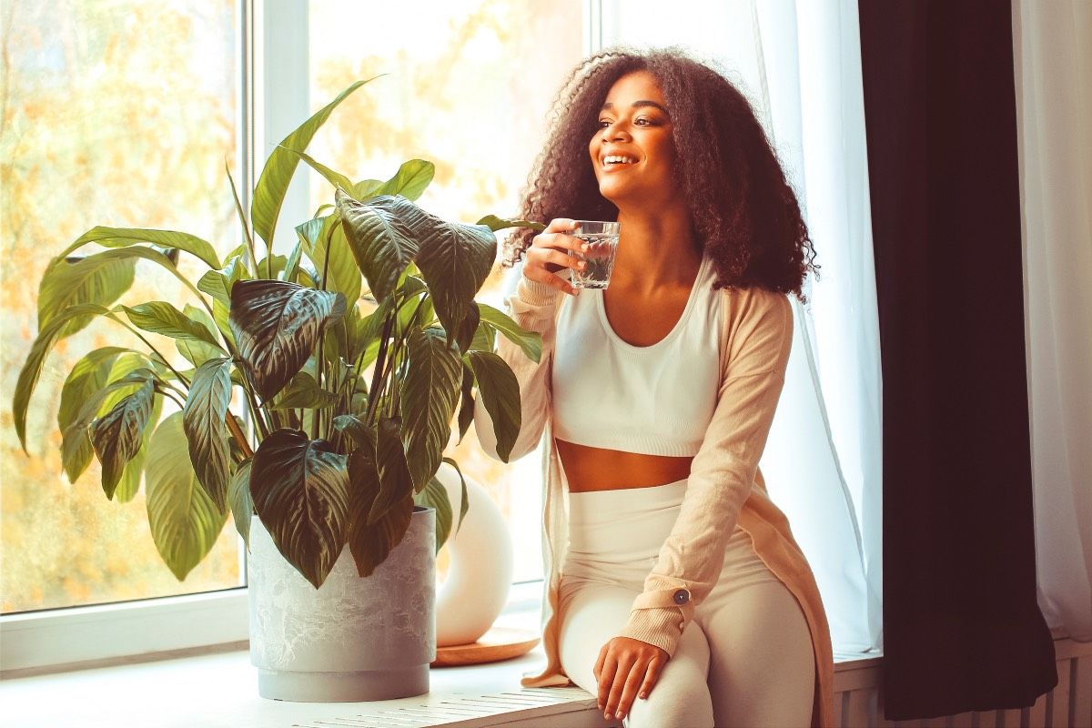 jeune femme avec un verre d'eau regardant sa fenêtre notion de bonne hygiène de vie